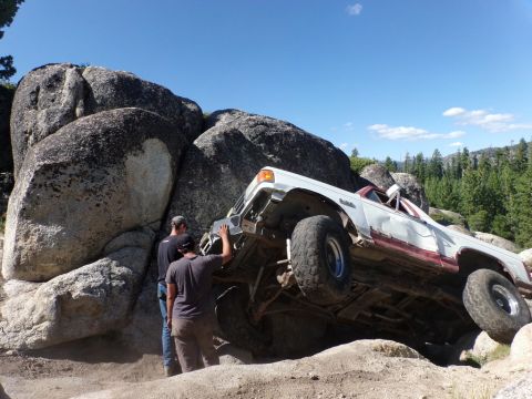 1984 Ford Bronco - Off-road vehicle navigates a rocky terrain, with onlookers observing its precarious position.