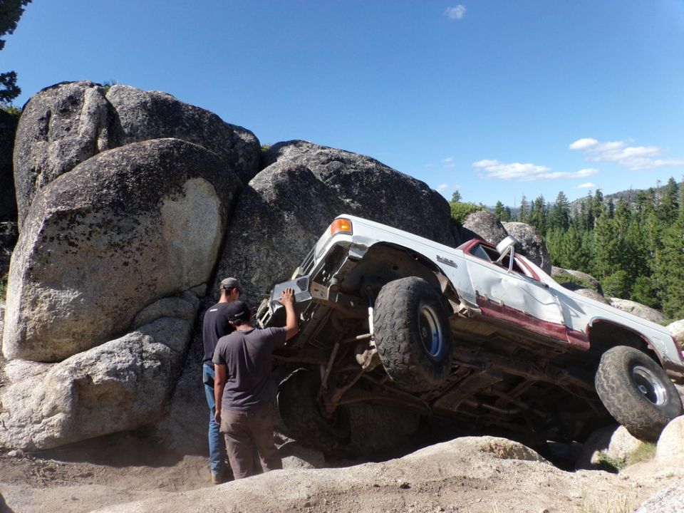 White and red off-road vehicle tilted on rocks with people nearby