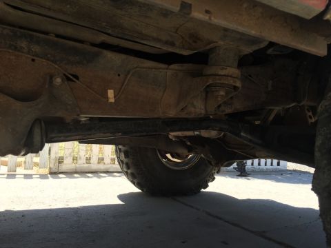 1984 Ford Bronco - The underside of a vehicle is shown, focusing on the frame, suspension components, and a tire. The vehicle appears to be an older model tru…