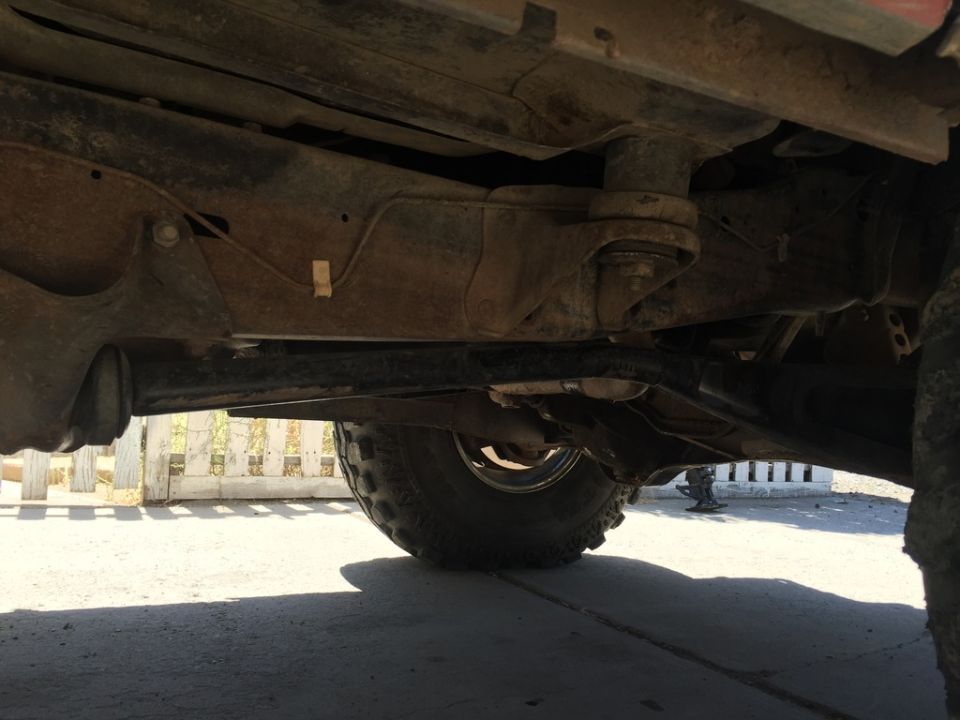 Underside view of a vehicle frame, suspension, and tire, showing rust and wear.