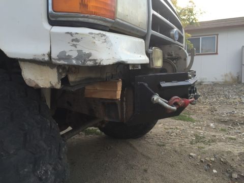 1984 Ford Bronco - The front bumper of a white Ford Bronco has been modified with a black steel winch bumper that includes a red tow hook. The vehicle is park…