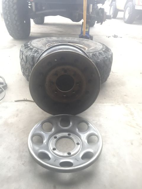 1984 Ford Bronco - A close-up view shows a steel wheel rim and a silver hubcap on a concrete surface, with a tire and part of a vehicle in the background.