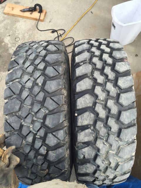 1984 Ford Bronco - Two large, aggressive off-road tires are shown side-by-side on a concrete surface. A black power cord and a yellow extension cord are visib…