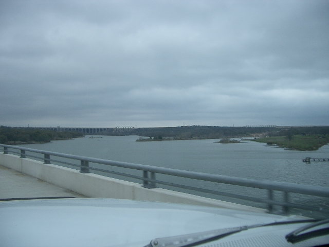 View of a large dam across a lake from a bridge. Cloudy sky
