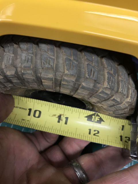 1989 Ford Bronco - A measuring tape is placed next to the tire of a yellow vehicle, indicating a measurement between 10 and 13 inches.