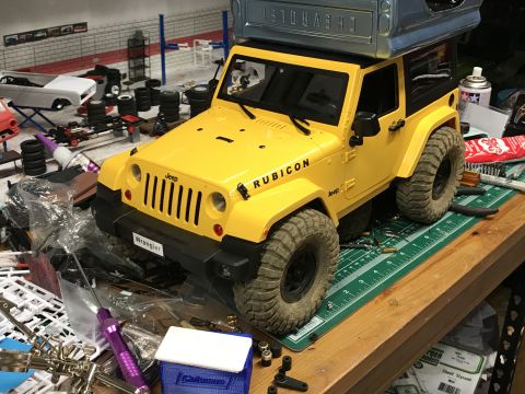 1989 Ford Bronco - A detailed remote-controlled Jeep Wrangler Rubicon model is displayed on a workbench amidst various hobby supplies.