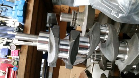 1981 Ford Bronco - A close-up, side-angle view of a polished metal crankshaft with multiple counterweights. The crankshaft is resting on a wooden surface, wit…