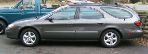 2003 Ford Taurus - A gray 2003 Ford Taurus station wagon is seen from the side, parked next to a teal pickup truck.