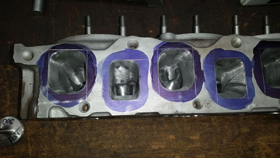 Engine cylinder head with intake ports outlined in purple marker for porting. A small circular object with writing is visible to the left