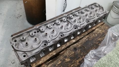 1981 Ford Bronco - An engine cylinder head rests on rough wooden beams in a workshop setting.