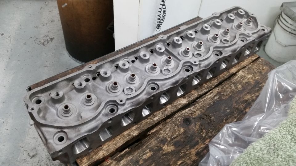 Aluminum engine cylinder head on wooden beams, with visible ports and valves
