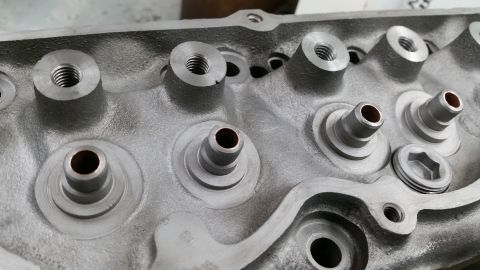 1981 Ford Bronco - Close-up view of the top of a cast aluminum engine cylinder head, showing threaded bolt holes and valve stems.