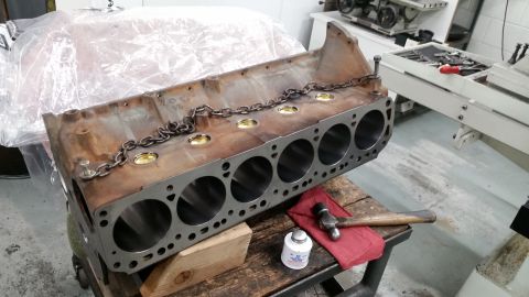 1981 Ford Bronco - A disassembled V8 engine block with a chain draped across the top sits on a wooden workbench. A hammer, red cloth, and a small bottle of se…