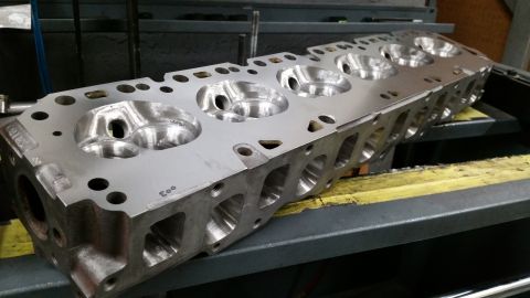 1981 Ford Bronco - A close-up, angled view of a machined aluminum V8 engine cylinder head with multiple intake and exhaust ports visible. The cylinder head is…