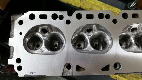1981 Ford Bronco - A close-up, overhead view of a polished aluminum engine cylinder head with two sets of intake and exhaust ports. The ports show machining m…