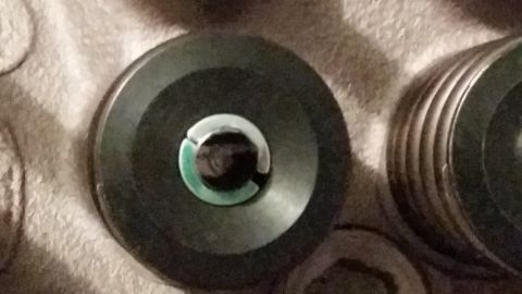 1981 Ford Bronco - A close-up, overhead view shows two dark-colored, circular automotive parts. The part on the left has a green and silver accent in its cent…