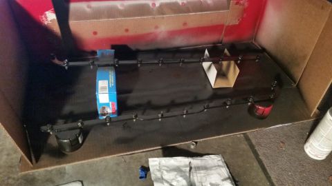 1981 Ford Bronco - A car part is being spray painted black inside a cardboard box. A blue box and some cardboard pieces are also visible.
