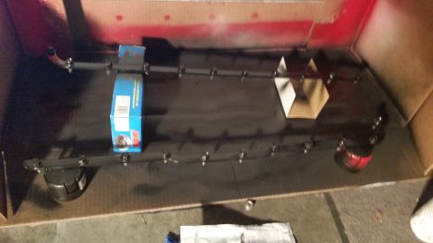 1981 Ford Bronco - A long, dark-colored automotive part, possibly a fuel rail or intake manifold, is laid out on a black surface inside a cardboard box. Sever…