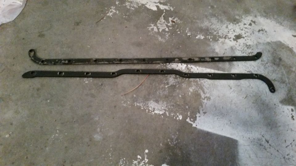 Two L-shaped metal brackets with holes on a concrete floor