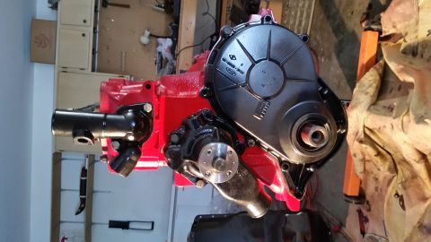 1981 Ford Bronco - A red engine block with a black timing cover and a black water pump is shown in a workshop setting. The engine appears to be a Ford, with v…