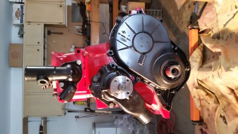 1981 Ford Bronco - A red engine block is assembled with a black water pump and a black timing cover. The engine is on a stand in a workshop setting.
