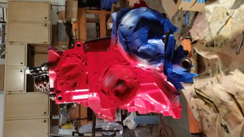 1981 Ford Bronco - A red engine block is partially covered with blue painter's tape. The engine appears to be in a workshop setting with cabinets and tools vi…