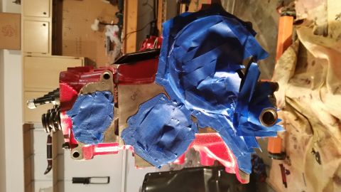 1981 Ford Bronco - A red engine block with brass components is covered in blue painter's tape, likely in preparation for painting or cleaning. The engine appe…