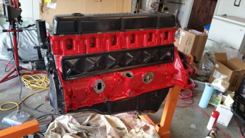 1981 Ford Bronco - A freshly painted red and black V8 engine is mounted on an orange engine stand in a garage. Various automotive supplies and boxes are visib…