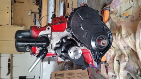 1981 Ford Bronco - A red engine block with a black timing cover and a black water pump is shown. A silver metal pipe extends from the front of the engine.