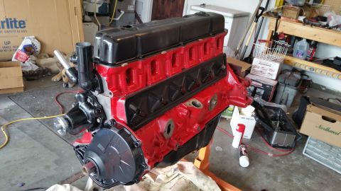 1981 Ford Bronco - A freshly painted red and black engine block is mounted on an orange engine stand in a garage setting. Various tools, storage containers, a…