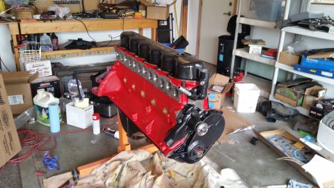 1981 Ford Bronco - A red engine block with a black valve cover sits on an engine stand in a garage. Various tools, parts, and supplies are scattered around th…