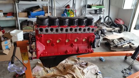 1981 Ford Bronco - A red engine block with black valve covers is mounted on an orange engine stand. Various automotive parts and storage shelves are visible i…