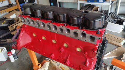 1981 Ford Bronco - A freshly painted red V8 engine block with a black valve cover is mounted on an orange engine stand. The engine appears to be in a garage o…