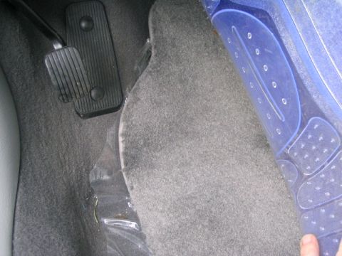 2003 Ford Taurus - The interior floor of a car shows gray carpet and black pedals, with a blue plastic mat partially covering the floor.