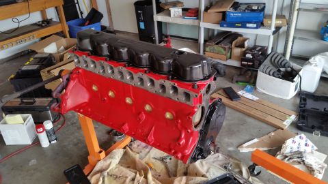 1981 Ford Bronco - A red and black engine block assembly is mounted on an orange engine stand in a garage setting. Various tools and automotive parts are scat…