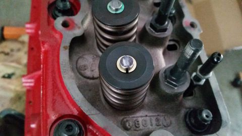 1981 Ford Bronco - A close-up view of a red engine block with a grey cylinder head. Several valve springs and retainers are visible, along with various bolts…