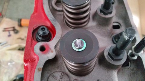1981 Ford Bronco - A close-up view of a red engine cylinder head with various components installed, including valve springs, retainers, and bolts. The engine…