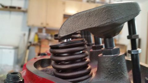 1981 Ford Bronco - A close-up, angled view of a valve spring and rocker arm assembly on a red engine block. The assembly is made of dark metal with visible bo…