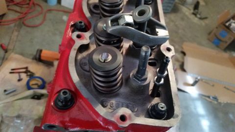 1981 Ford Bronco - A close-up view of the top of a red engine cylinder head, showing valve springs, rocker arms, and bolts. Several parts are installed, sugge…