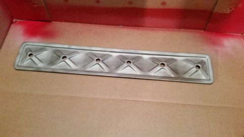 1981 Ford Bronco - A metal valve cover with a diamond pattern and five bolt holes is shown in a cardboard box with red spray paint splatter on the sides.