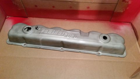 1981 Ford Bronco - A silver-colored Ford valve cover with raised lettering that reads "POWER BY FORD" is shown in a spray-painting booth. The valve cover is r…