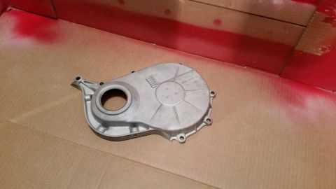 1981 Ford Bronco - A silver engine timing cover is shown resting on a cardboard surface, with red spray paint visible in the background. The cover has embosse…