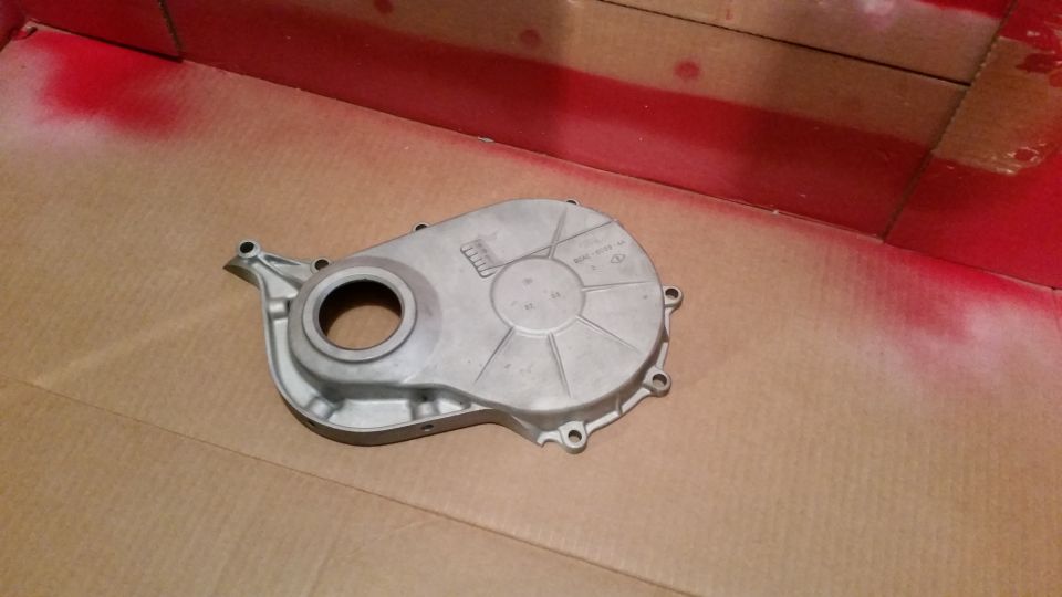 Silver engine timing cover with embossed text on cardboard