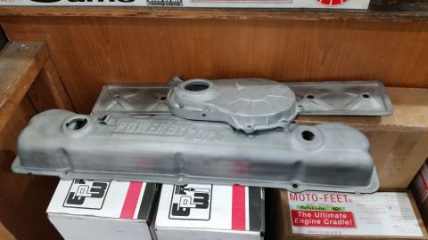 1981 Ford Bronco - Two unpainted aluminum valve covers and a timing cover are displayed on top of cardboard boxes. The larger valve cover has "POWER BY FORD"…