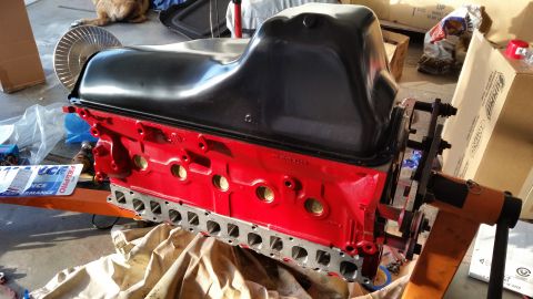 1981 Ford Bronco - A red engine block with a black oil pan is mounted on an engine stand. A silver fan is visible to the left of the engine.