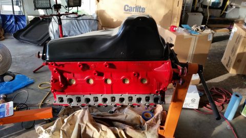 1981 Ford Bronco - A red engine block with a black oil pan is mounted on an orange engine stand. Various automotive parts and boxes are visible in the backgro…