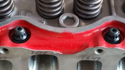 1981 Ford Bronco - A close-up view of a red-painted engine cylinder head with two black hex-head bolts visible. The cylinder head has markings indicating meas…