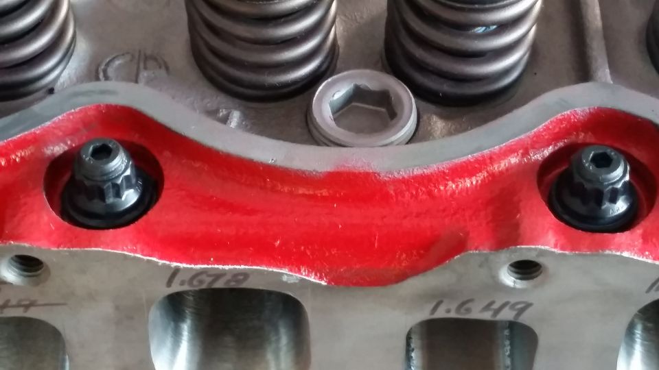 Close-up of a red-painted engine cylinder head with two black bolts and measurement markings.