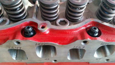 1981 Ford Bronco - A close-up view of a red-painted engine cylinder head with two black fasteners visible. Markings indicating valve sizes, such as "1.649" an…