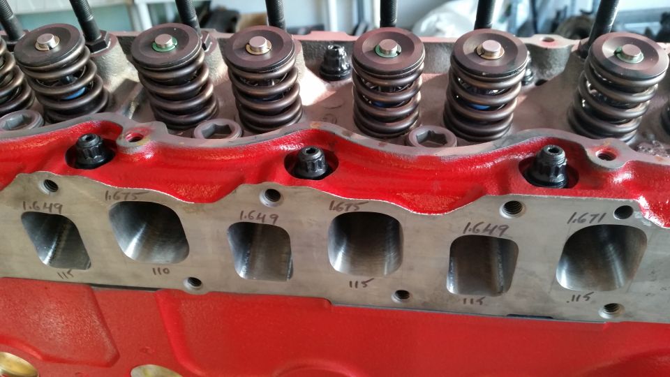 Red engine block with valve springs and intake ports labeled with measurements.